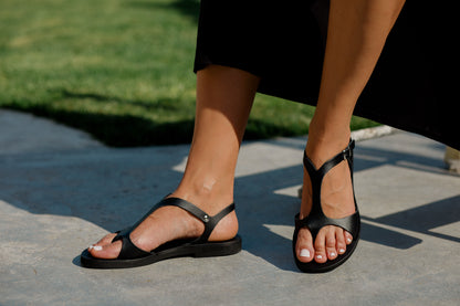 Woman wearing Stemma Greek Leather Sandals in black with T-bar design and toe loop
