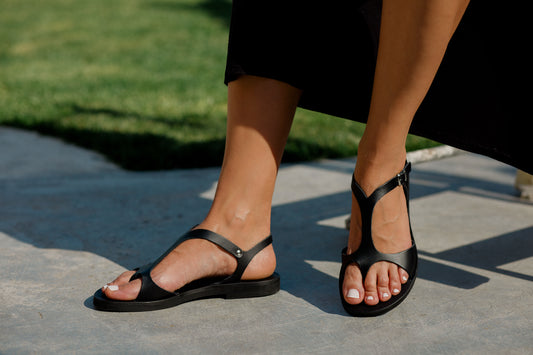 Woman wearing Stemma Greek Leather Sandals in black with T-bar design and toe loop
