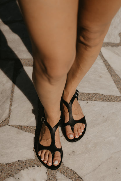 Woman wearing Stemma Greek Leather Sandals in black with T-bar design and toe loop
